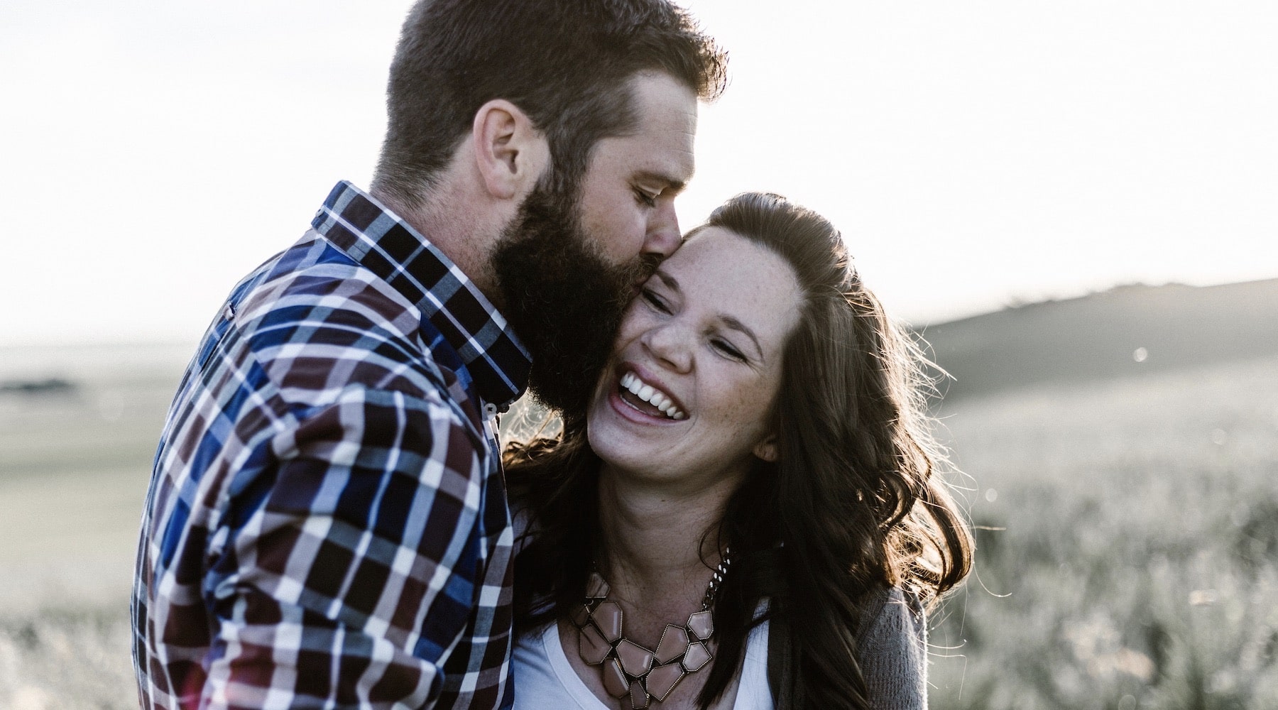 bearded man kissing a laughing woman on the cheek