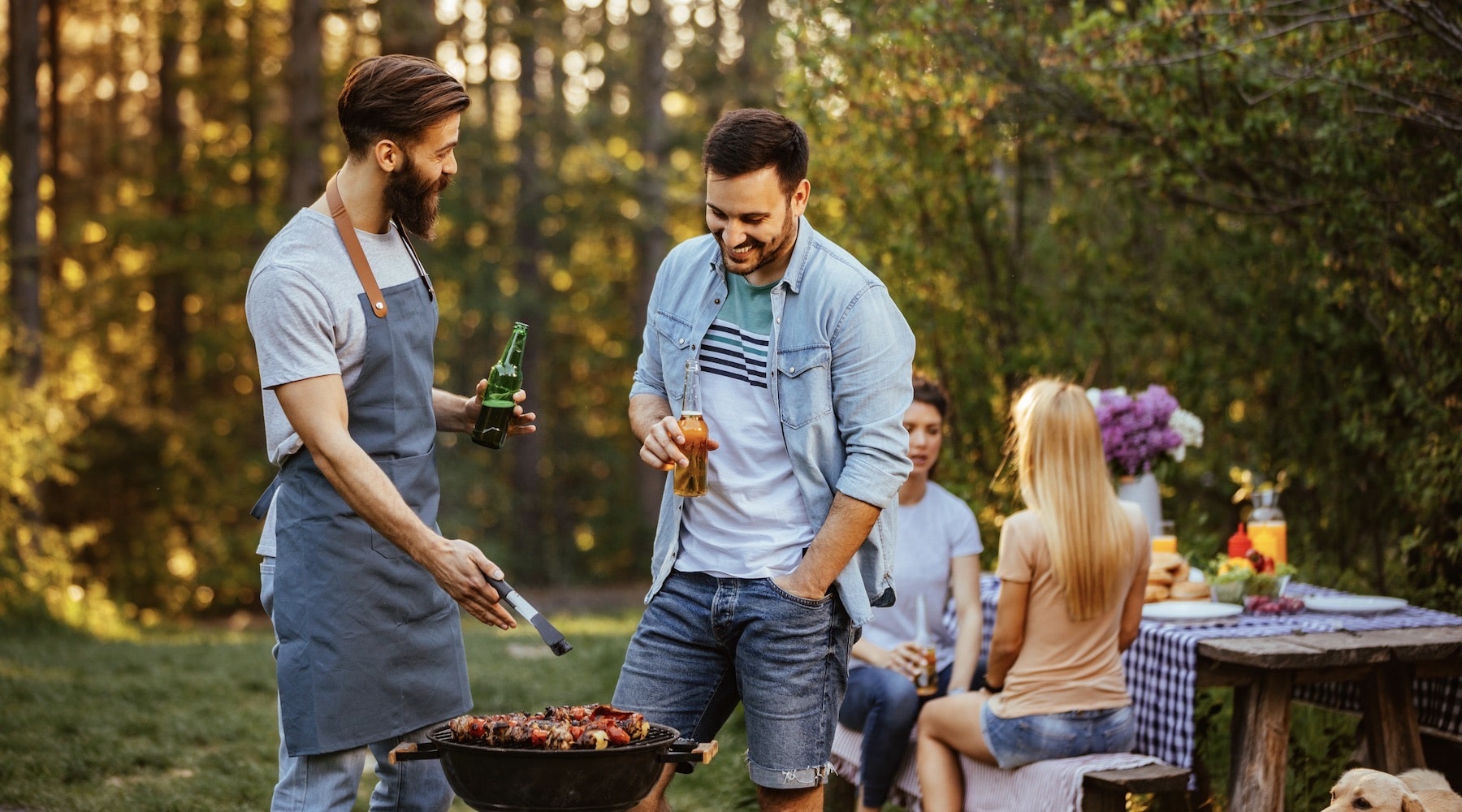 two bearded men laughing while having a beer at a bbq