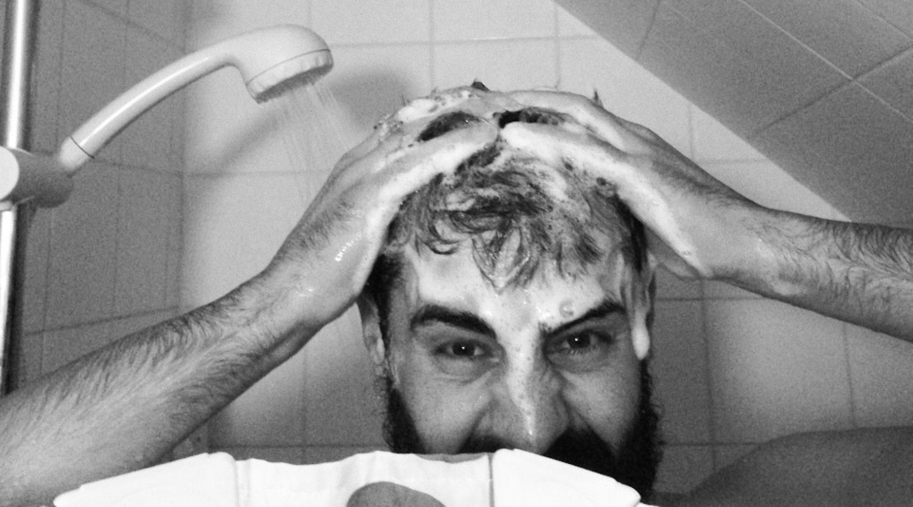 head and arms of a bearded man covered in beard shampoo suds whilst washin