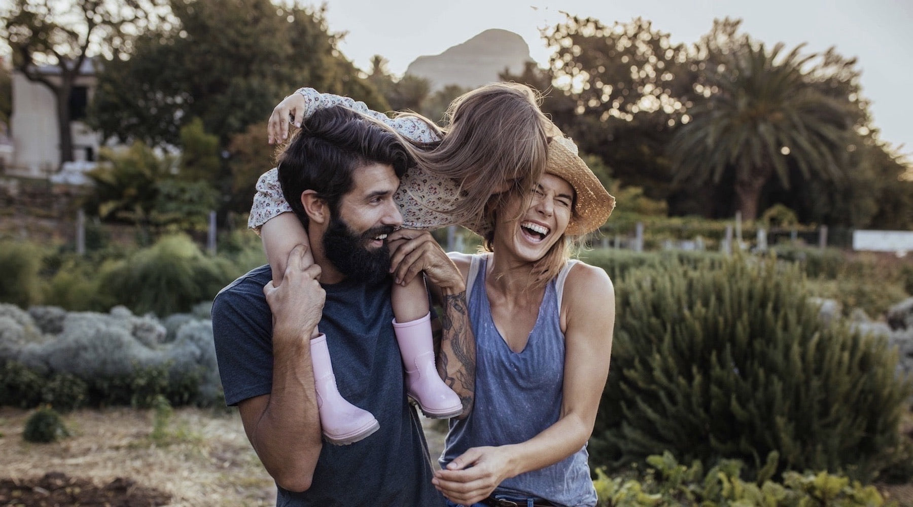 Bearded man with a young girl on his shoulders and a laughing women beside him enjoying a walk in the countryside