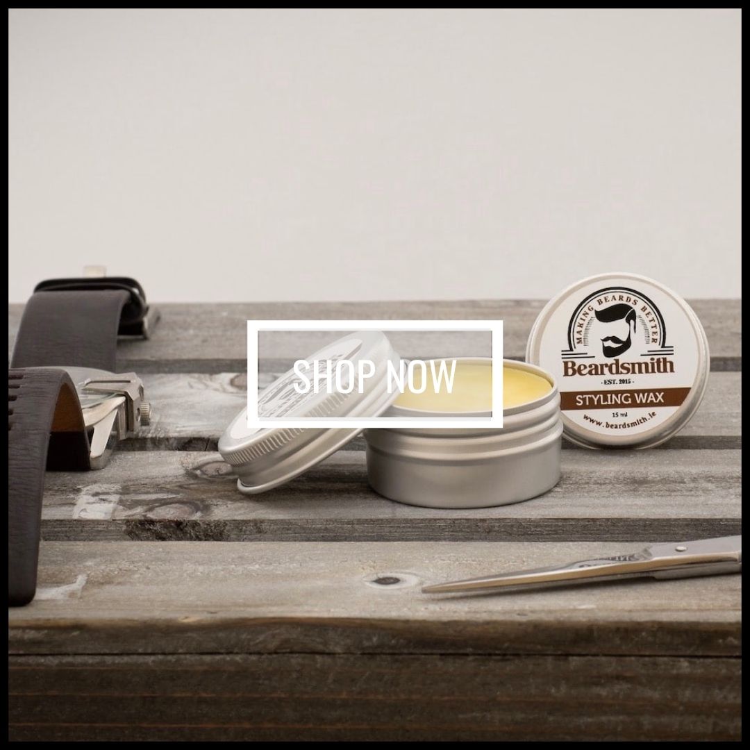 Tin of beard wax on a table with a watch and some scissors